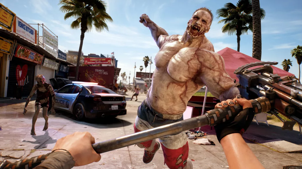 A first-person combat scene in Dead Island 2, showing the player facing a massive, muscular zombie lunging forward in a sunlit, post-apocalyptic Venice Beach setting.