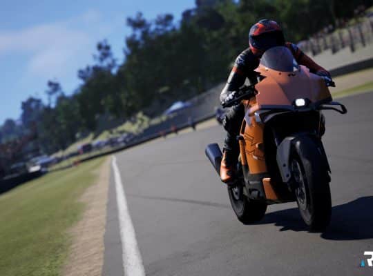 A realistic screenshot from the motorcycle racing game RIDE 6 showing a rider leaning into a turn on an orange sport bike on a paved race track with green grass and crowds in the background.