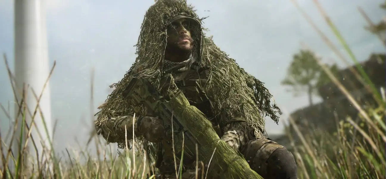 A close-up, dramatic shot of a soldier wearing a heavy ghillie suit and face paint, kneeling in tall grass with his sniper rifle, set against a blurred, slightly hazy background with a wind turbine.
