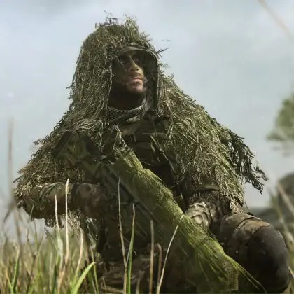 A close-up, dramatic shot of a soldier wearing a heavy ghillie suit and face paint, kneeling in tall grass with his sniper rifle, set against a blurred, slightly hazy background with a wind turbine.