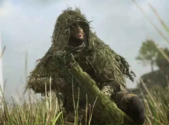 A close-up, dramatic shot of a soldier wearing a heavy ghillie suit and face paint, kneeling in tall grass with his sniper rifle, set against a blurred, slightly hazy background with a wind turbine.