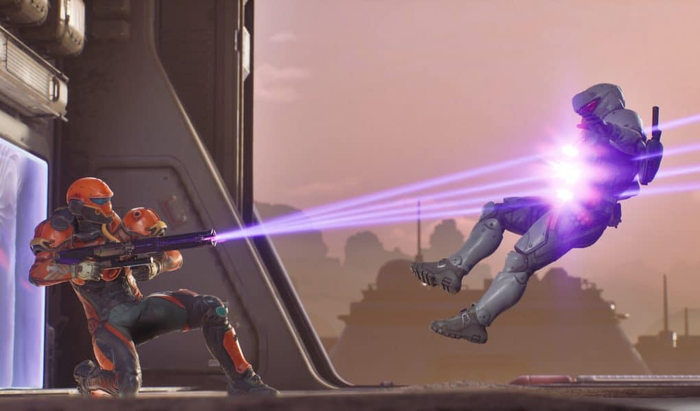 A futuristic third-person screenshot from Splitgate Arena Reloaded showing a player in orange and black armor firing a purple energy weapon at an opponent in white armor who is launched backward by the impact.