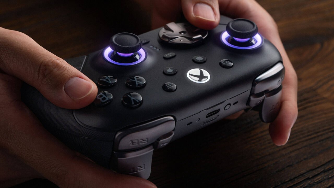 Hands holding the black 8BitDo Ultimate 3E Controller for Xbox, with purple RGB rings glowing around both thumbsticks
