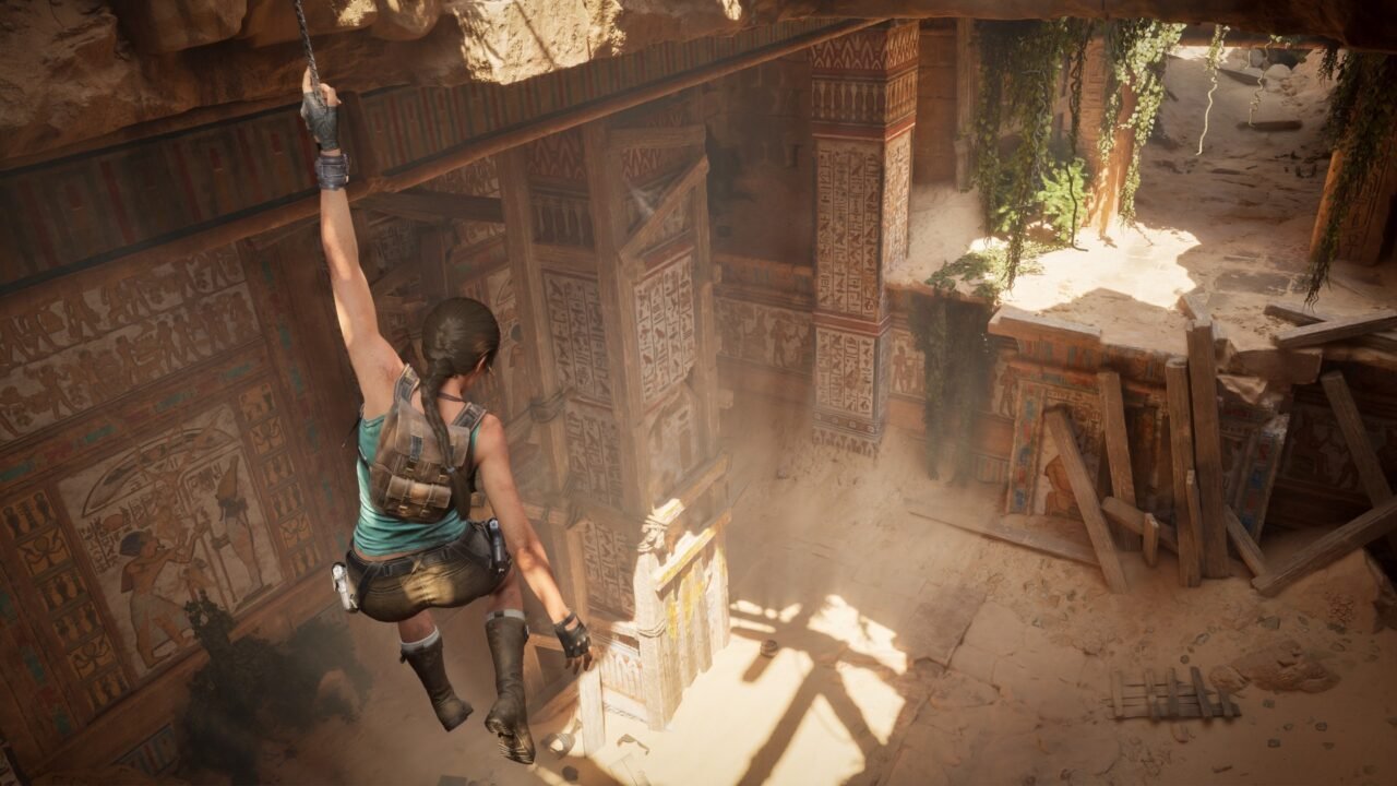 Lara Croft swinging from a rope inside a sunlit Egyptian tomb with painted hieroglyph walls in Tomb Raider: Legacy of Atlantis