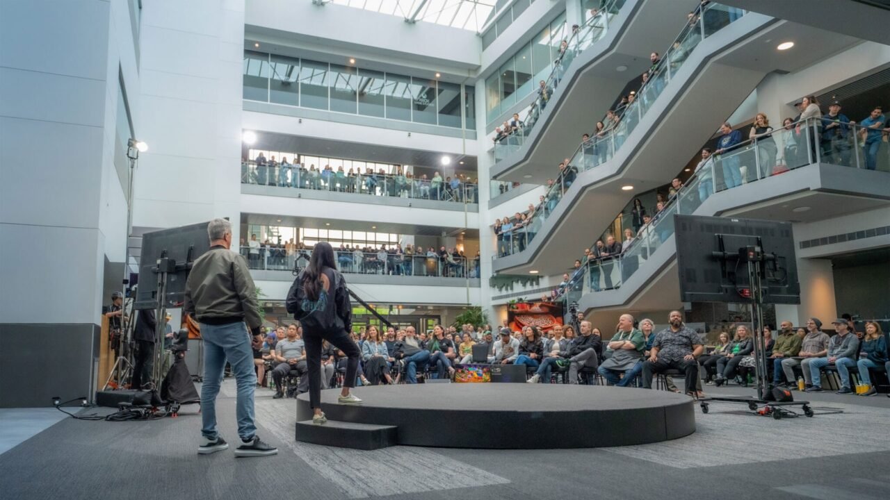 Xbox staff gathered on the balconies of a multi-storey atrium watching a speaker on a small stage