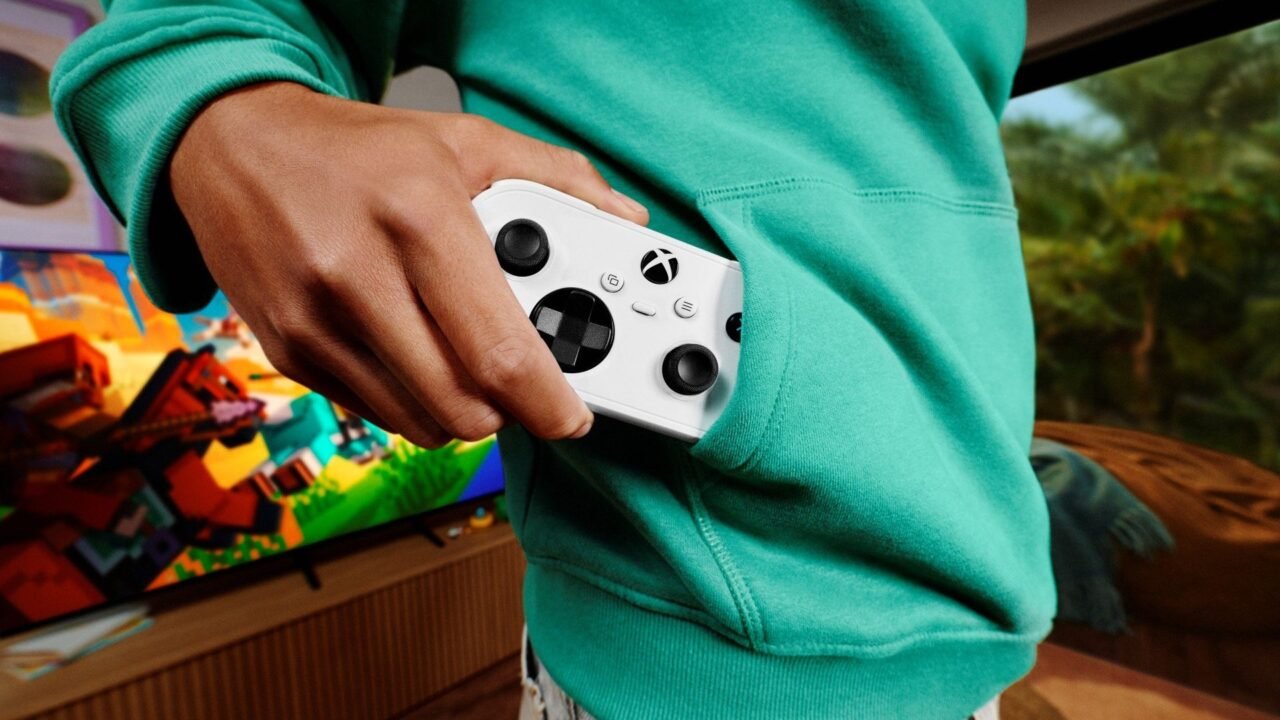 A player in a green hoodie holding a white Xbox controller in front of a TV