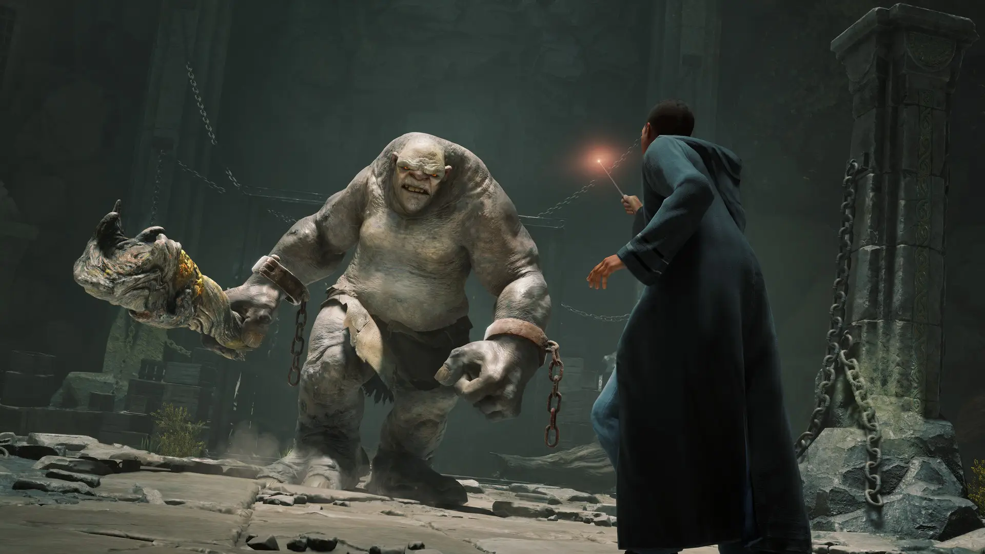 A dramatic screenshot from Hogwarts Legacy showing a student wizard in a dark dungeon facing off against a large, menacing, grey cave troll. The student is holding a wand that is emitting a faint glow.